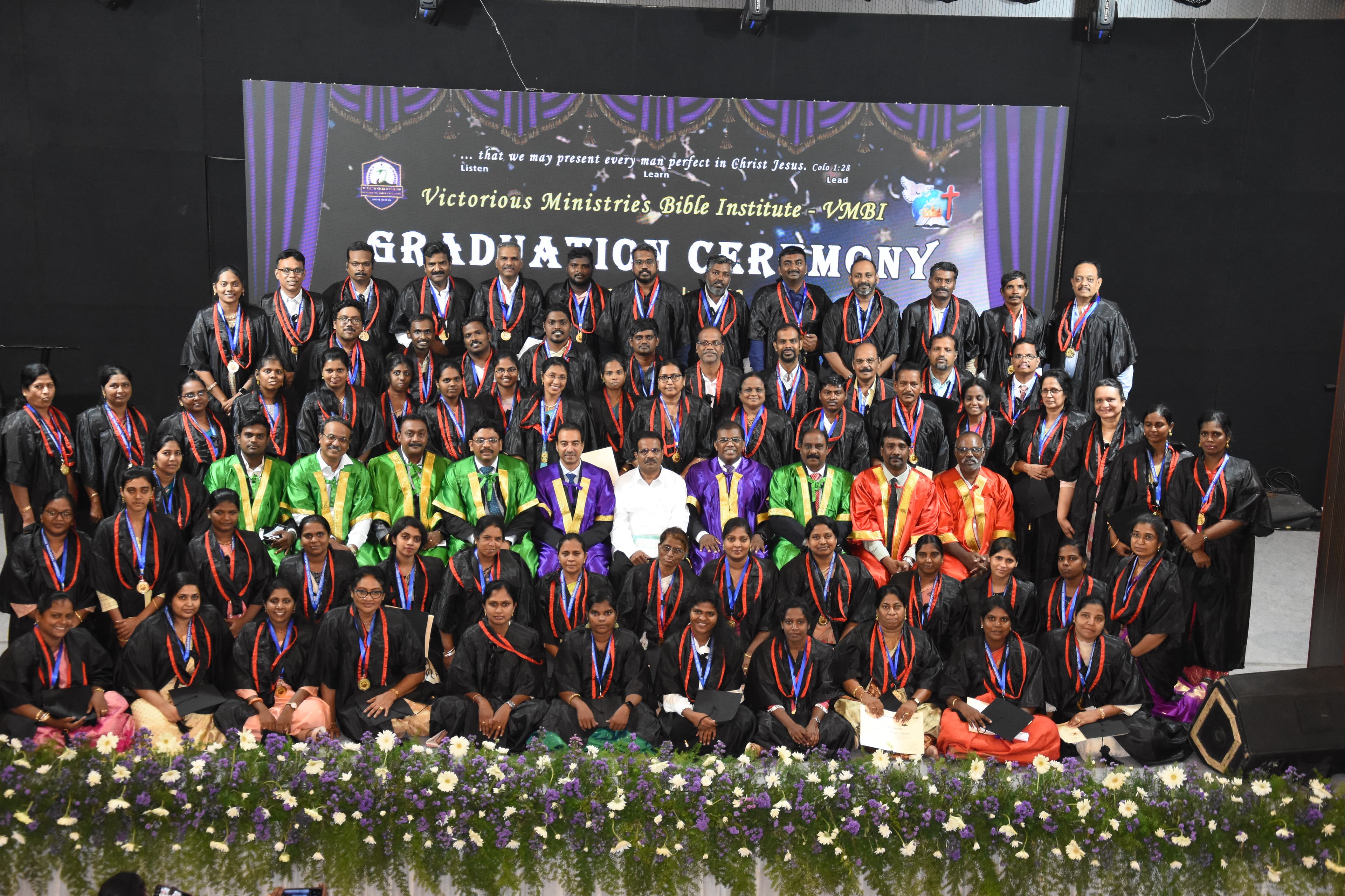 A full graduating group photographed on stage at the Bible Institute graduation ceremony.